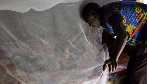 Father putting his daughter under a bednet in Burkina Faso - ©Jed Stone